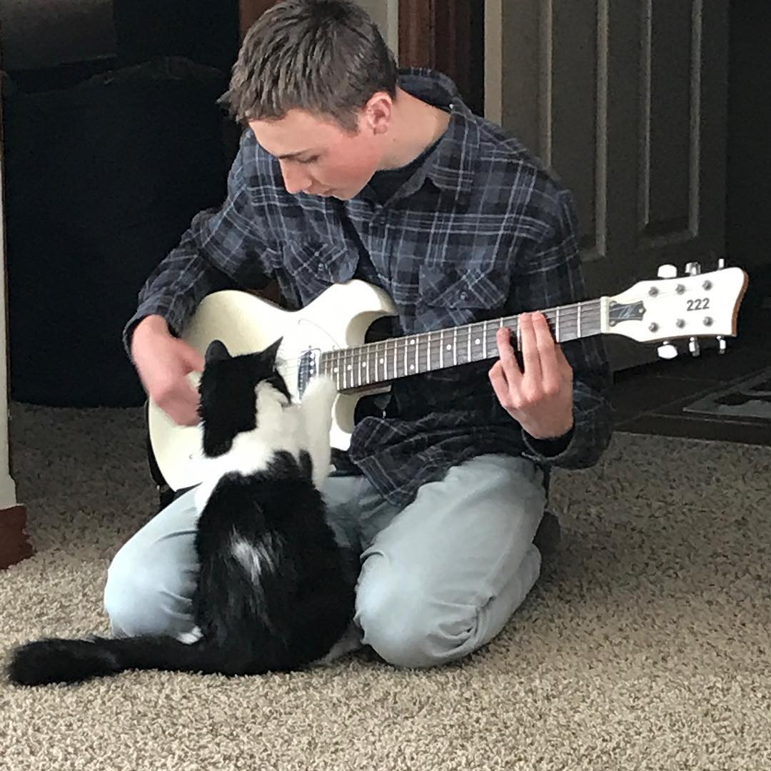 Picture of Isaac playing his guitar in front of his cat, Muzz